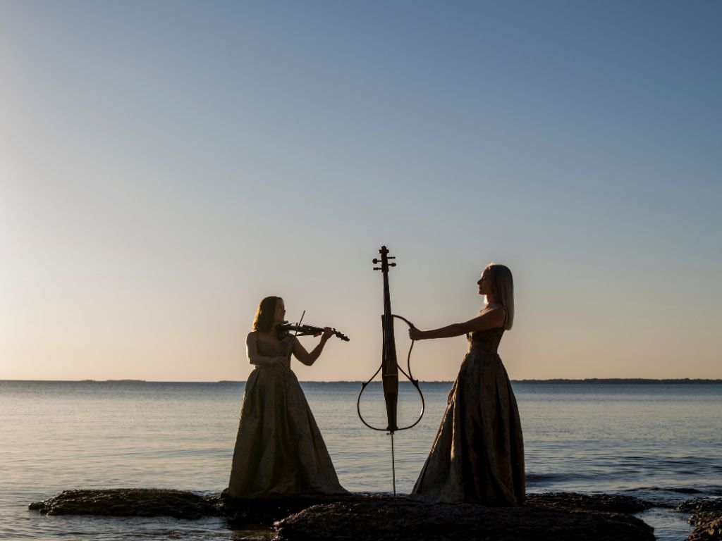 County Strings holding their electric instruments on rocks at Sandbanks Provincial Park
